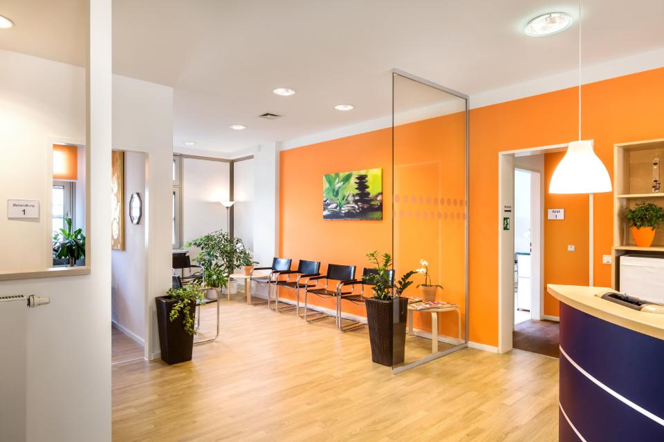 Blick in Wartebereich einer Praxis mit Stühlen vor einer orangen Wand, Hausarztpraxis Carmen Krüger